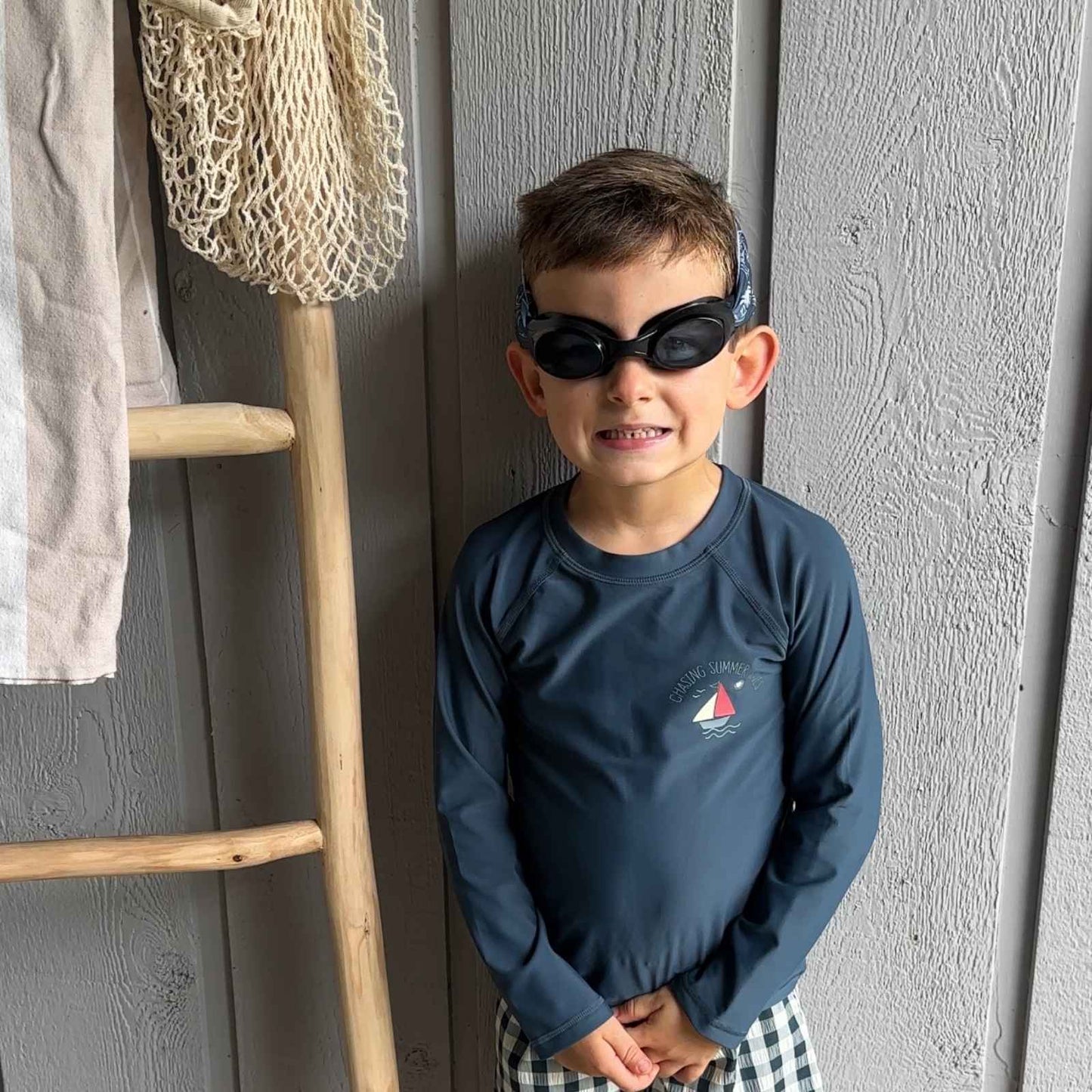 Child wearing fabric strap swim goggles standing next to a wooden ladder - Snappy Goggles