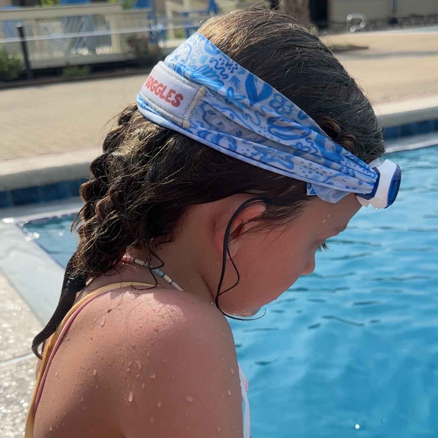 Child with a blue seashell fabric strap swim goggles by a pool - Snappy Goggles