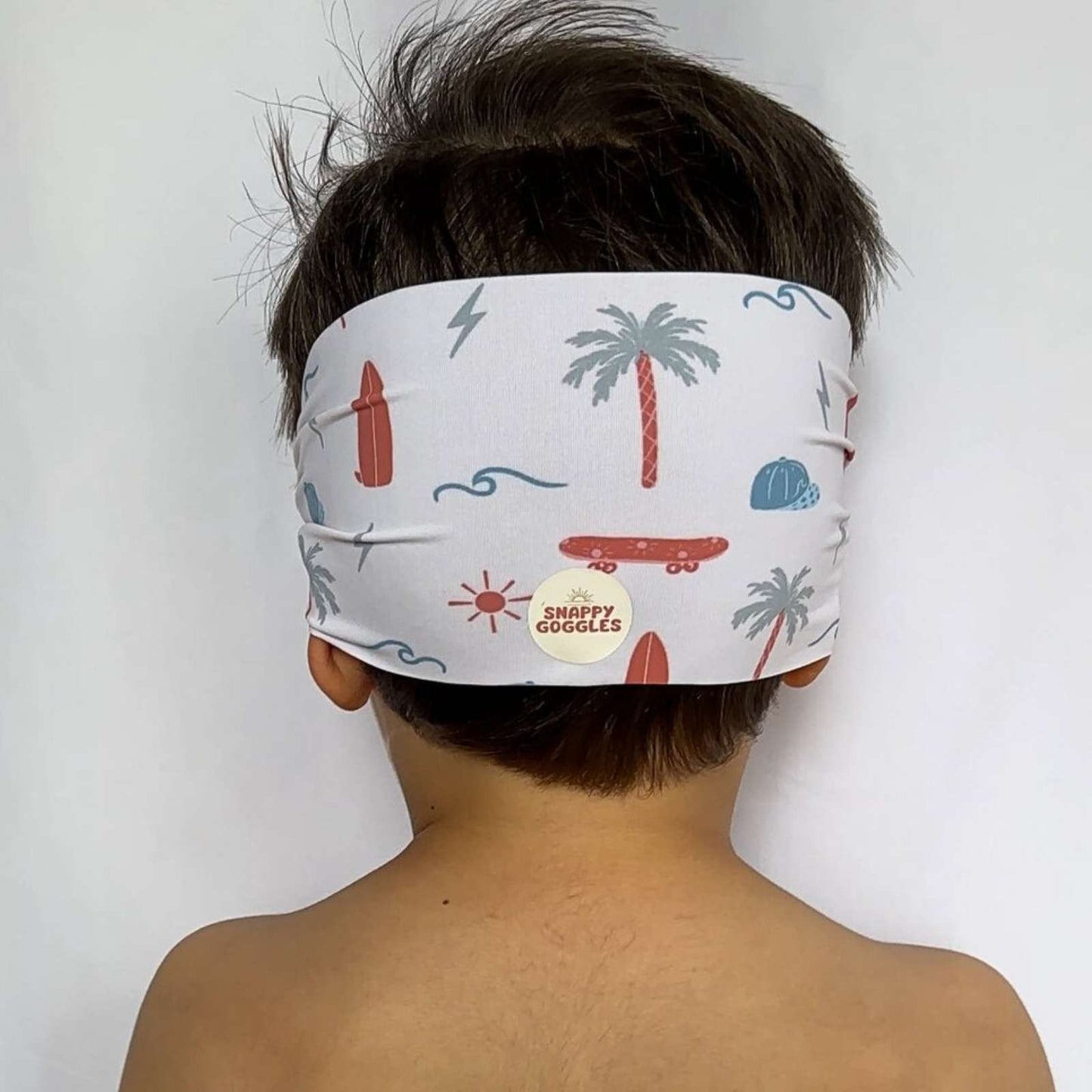back view of green and brown palm trees, orange skateboards and surf boards, with california vibe kid swim goggles with adjustable, fabric strap – Snappy Goggles
