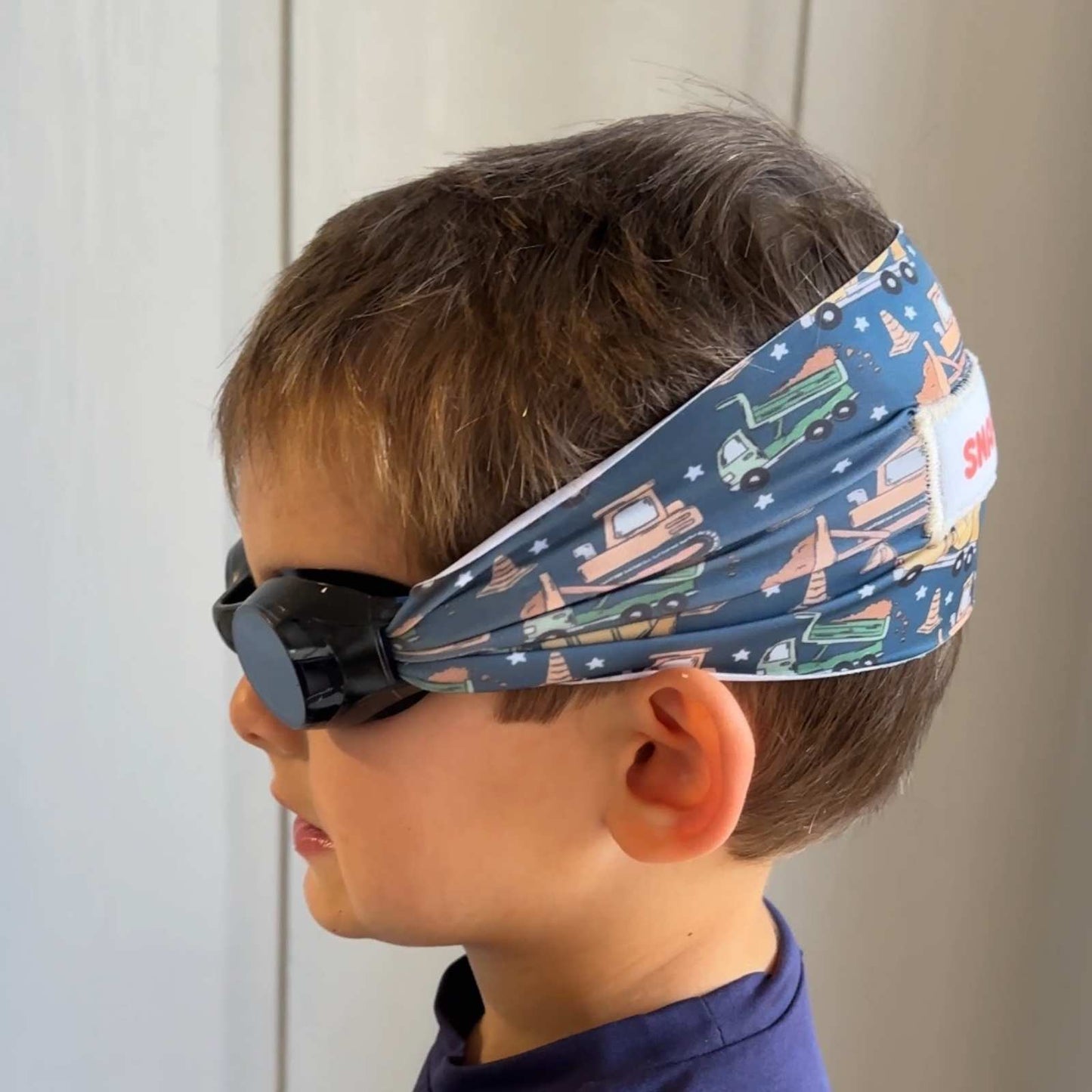 Child wearing a fabric swim goggles with construction vehicle pattern - Snappy Goggles