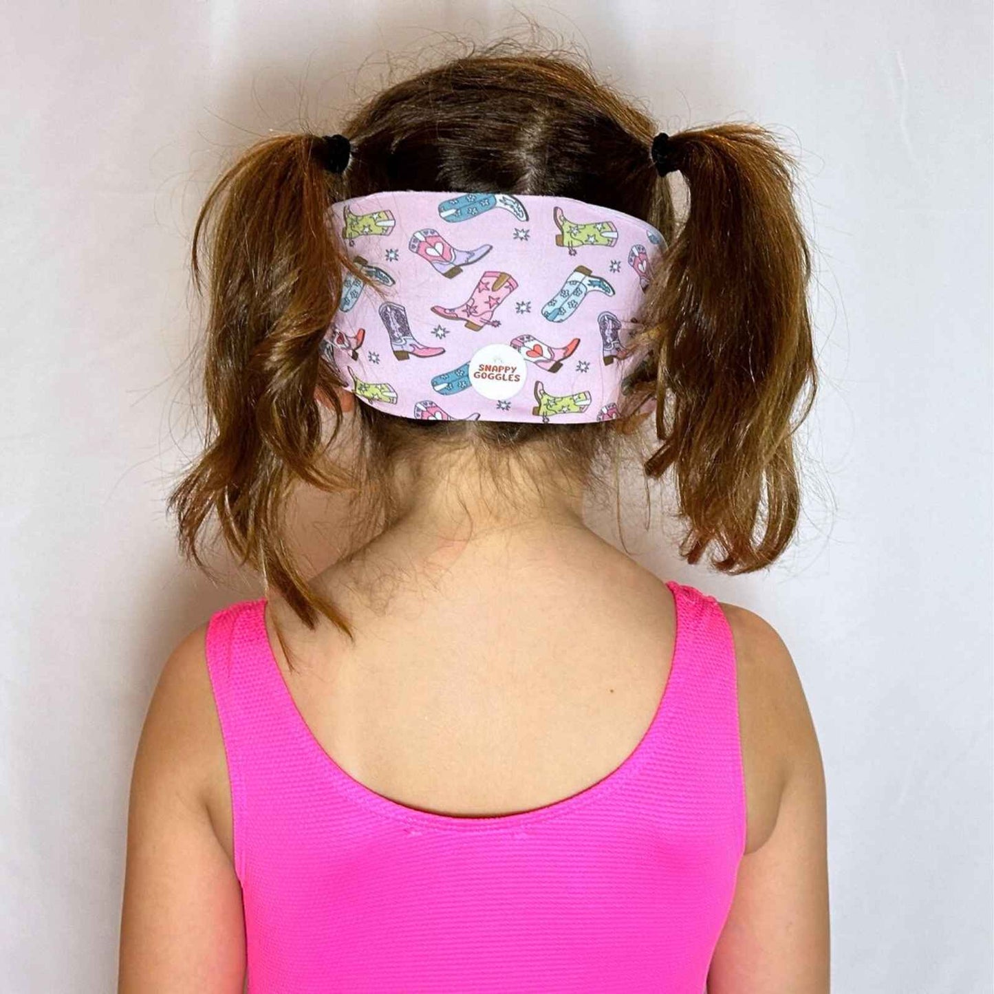 Girl wearing a fabric strap swim goggles with cowboy boot pattern and pink swimsuit - Snappy Goggles