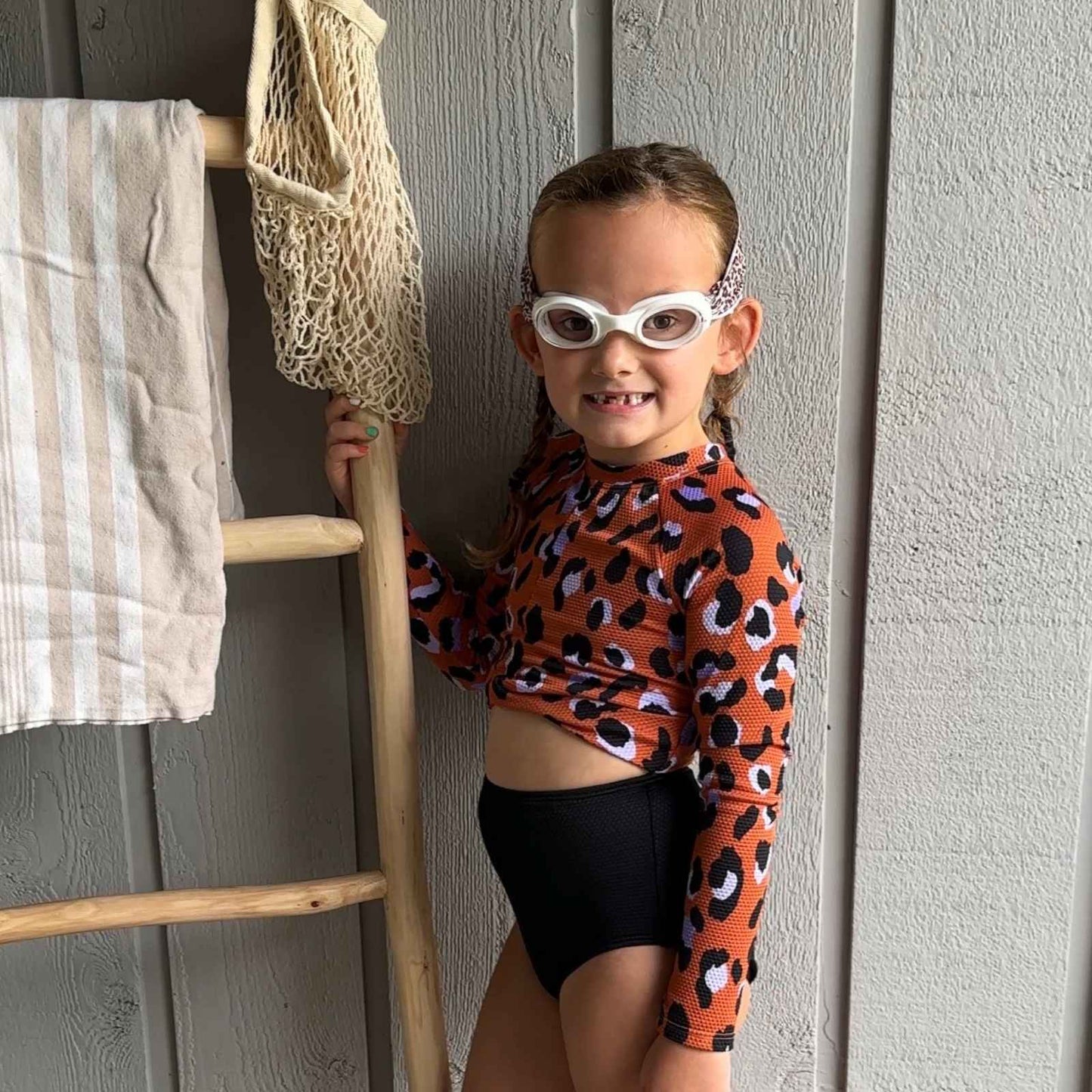 Child in a leopard print swimsuit wearing leopard fabric swim goggles smiling - Snappy Goggles