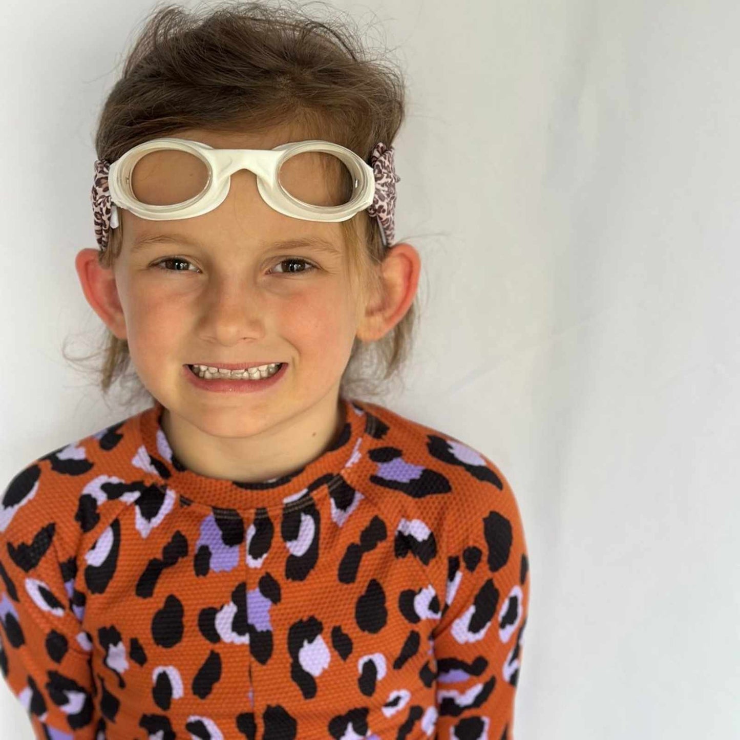 Child wearing a leopard fabric swim goggles on top of her head and smiling - Snappy Goggles