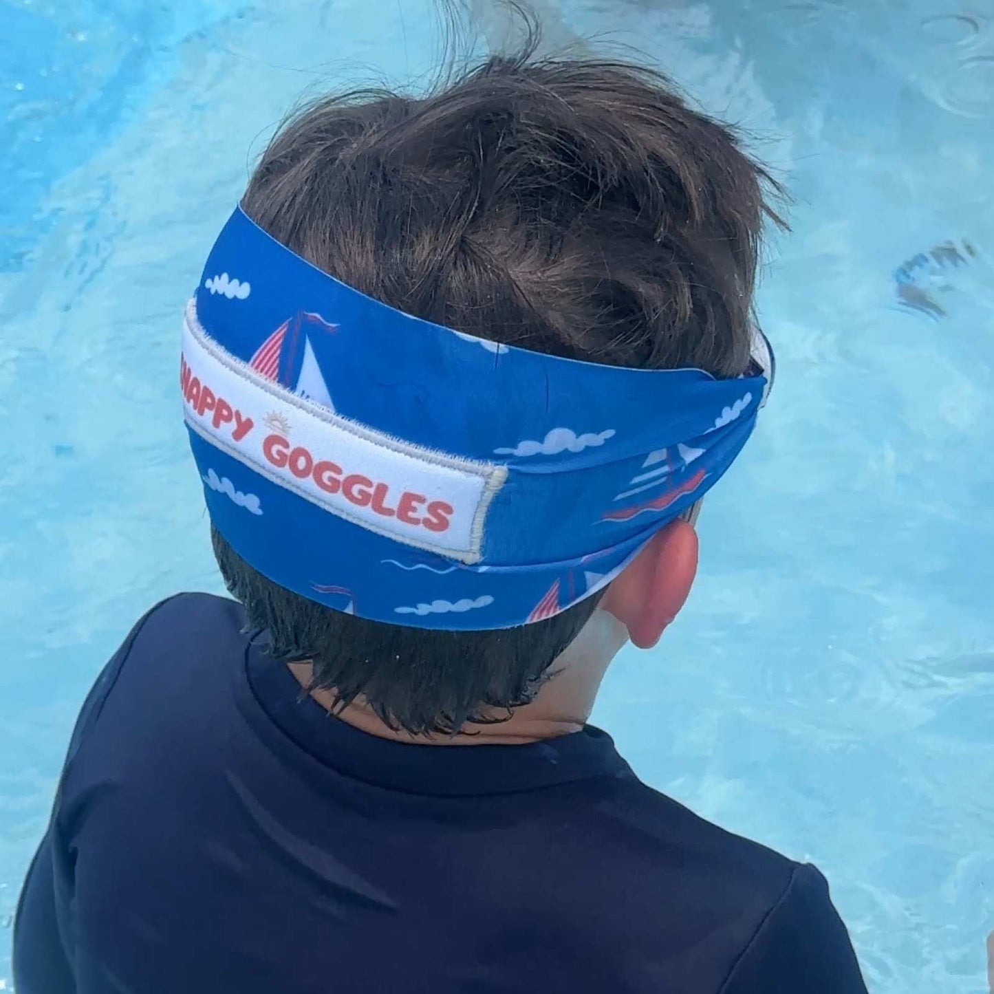 Child wearing a blue fabric strap swim goggles with 'Snappy Goggles' text in a pool.