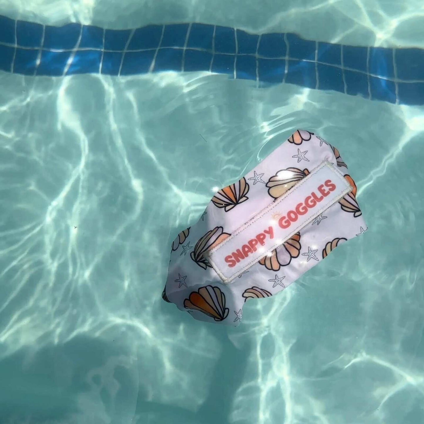 Snappy Goggles with pink shell pattern floating on top of the water