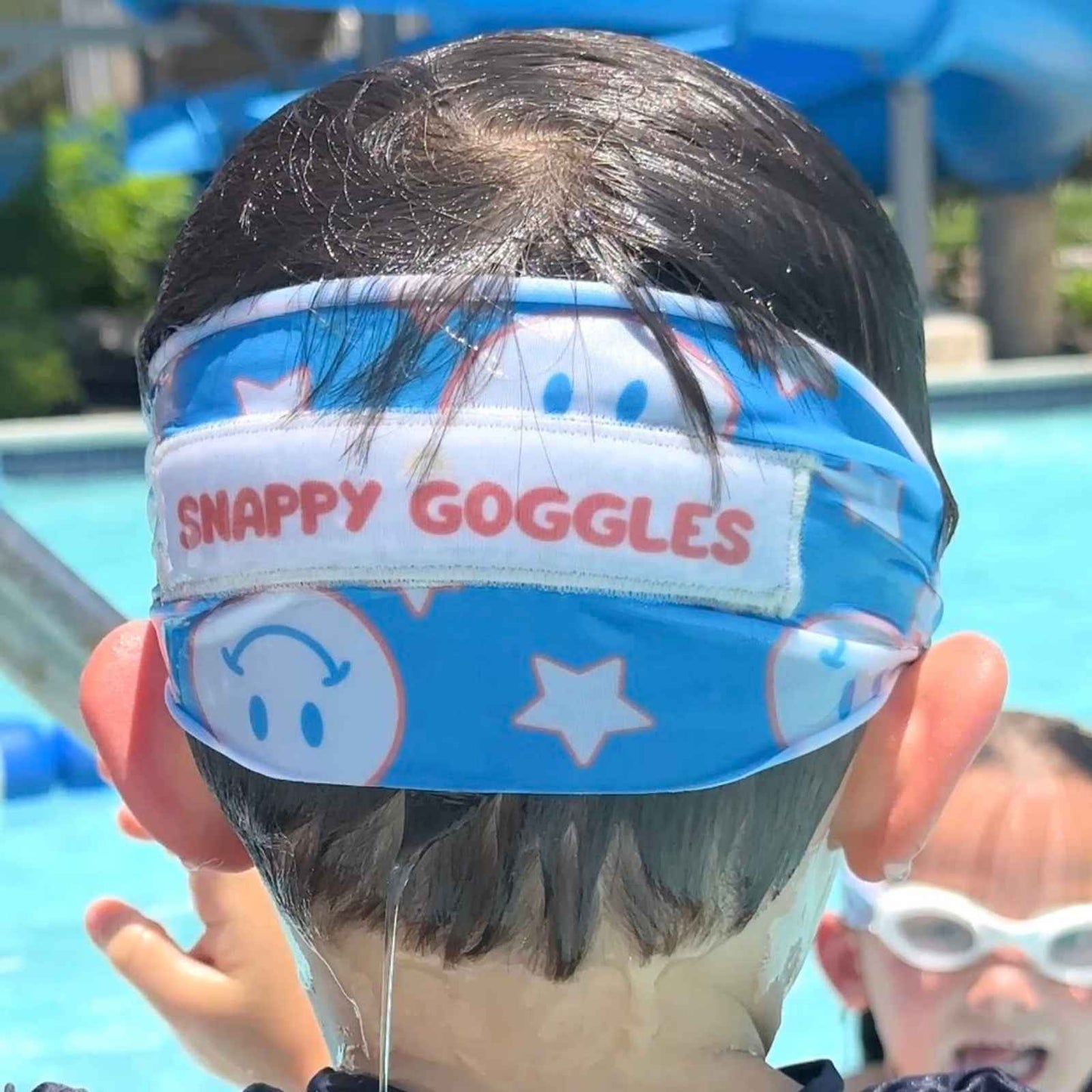 Child wearing blue and red smiley face and start fabric strap swim goggles in the pool - Snappy Goggles