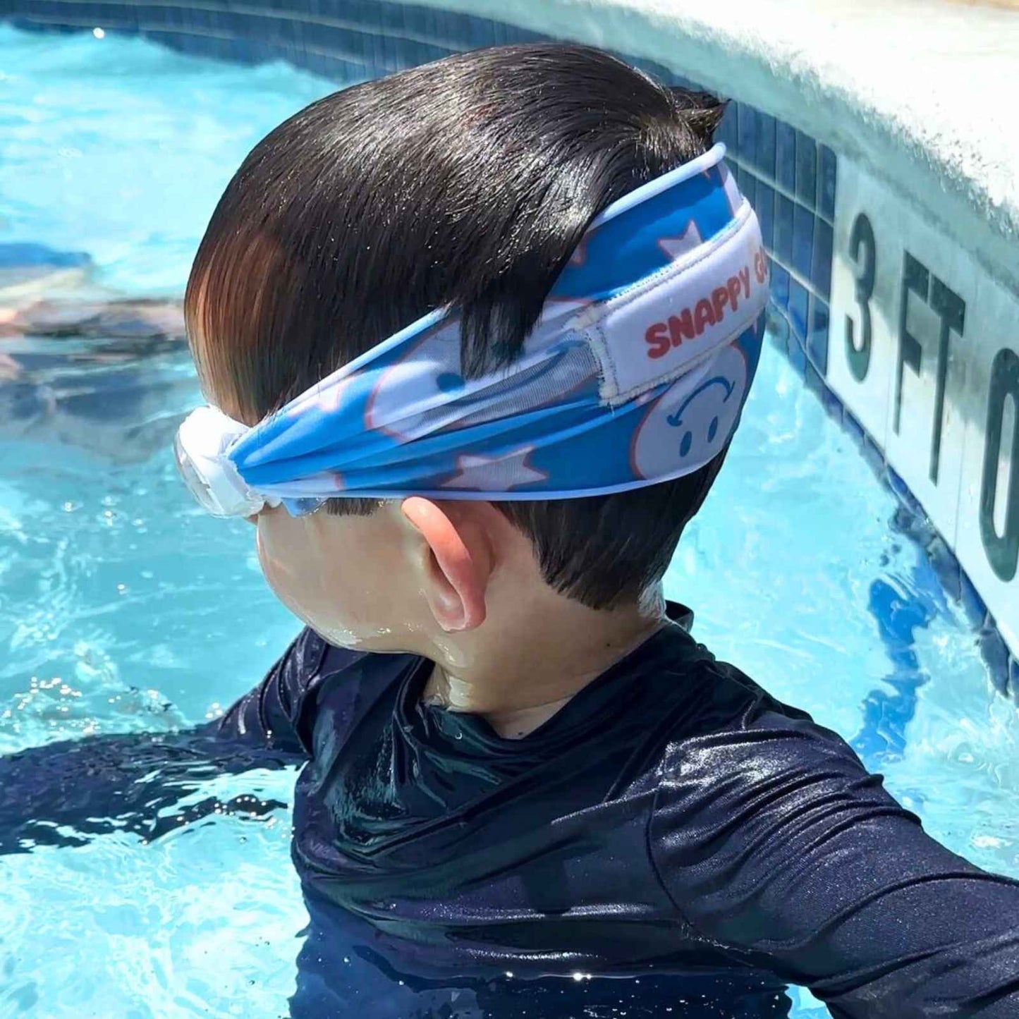 Child wearing a blue and red patriotic smiley face and stars pattern fabric swim goggles that don't pull hair in the pool - Snappy Goggles