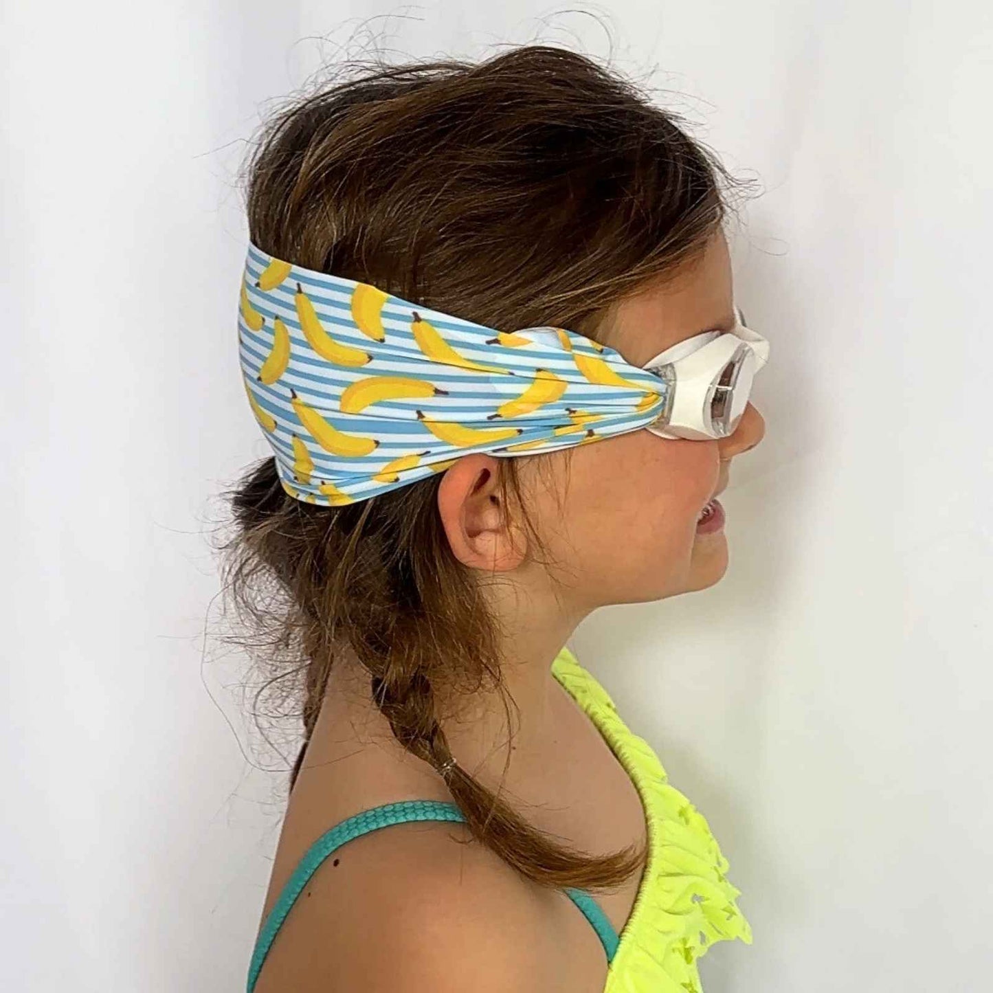 Child wearing a swim goggles with fabric strap with yellow banana pattern and blue and white stripes - Snappy Goggles