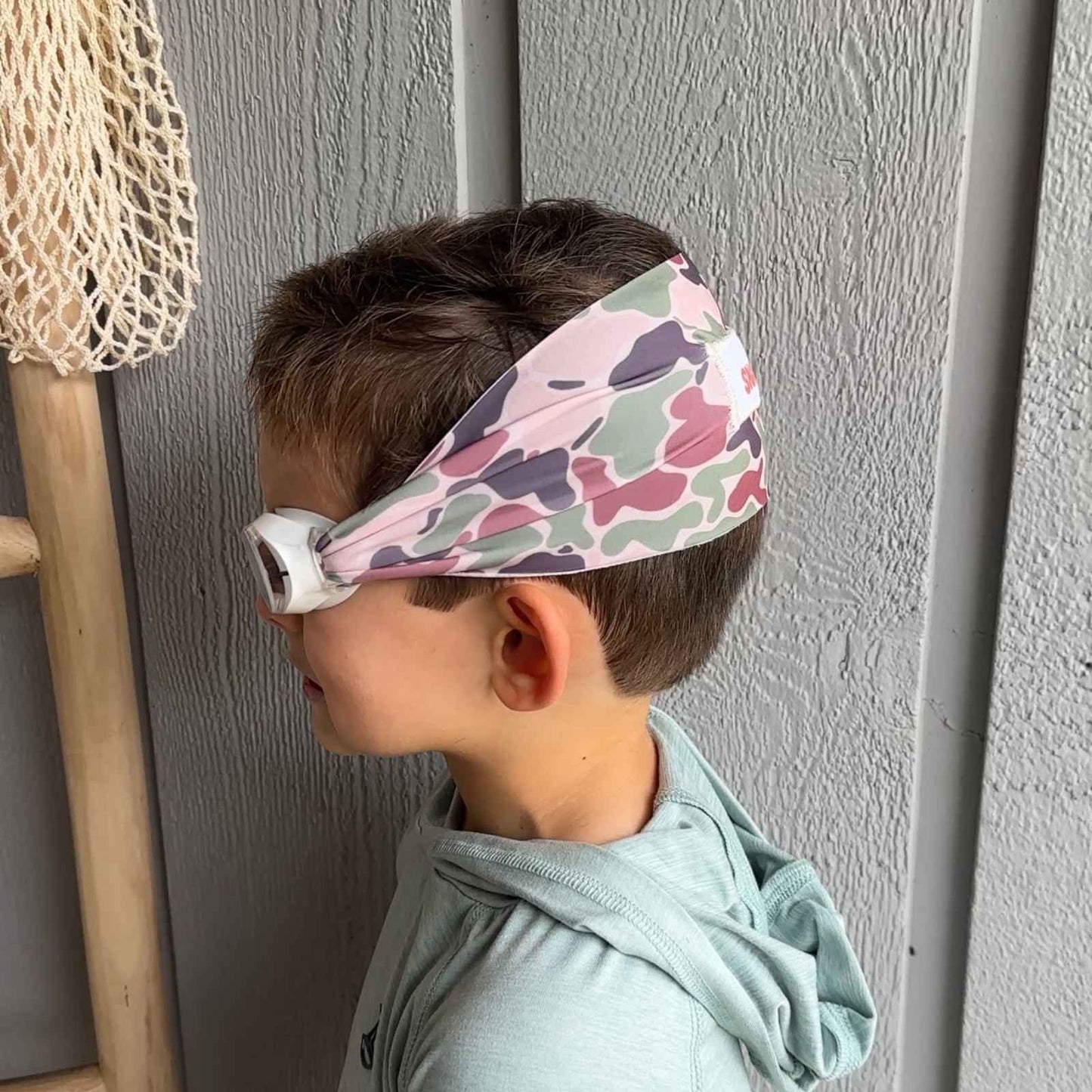 Child wearing a camo fabric swim goggles that don't pull or tangle hair - Snappy Goggles