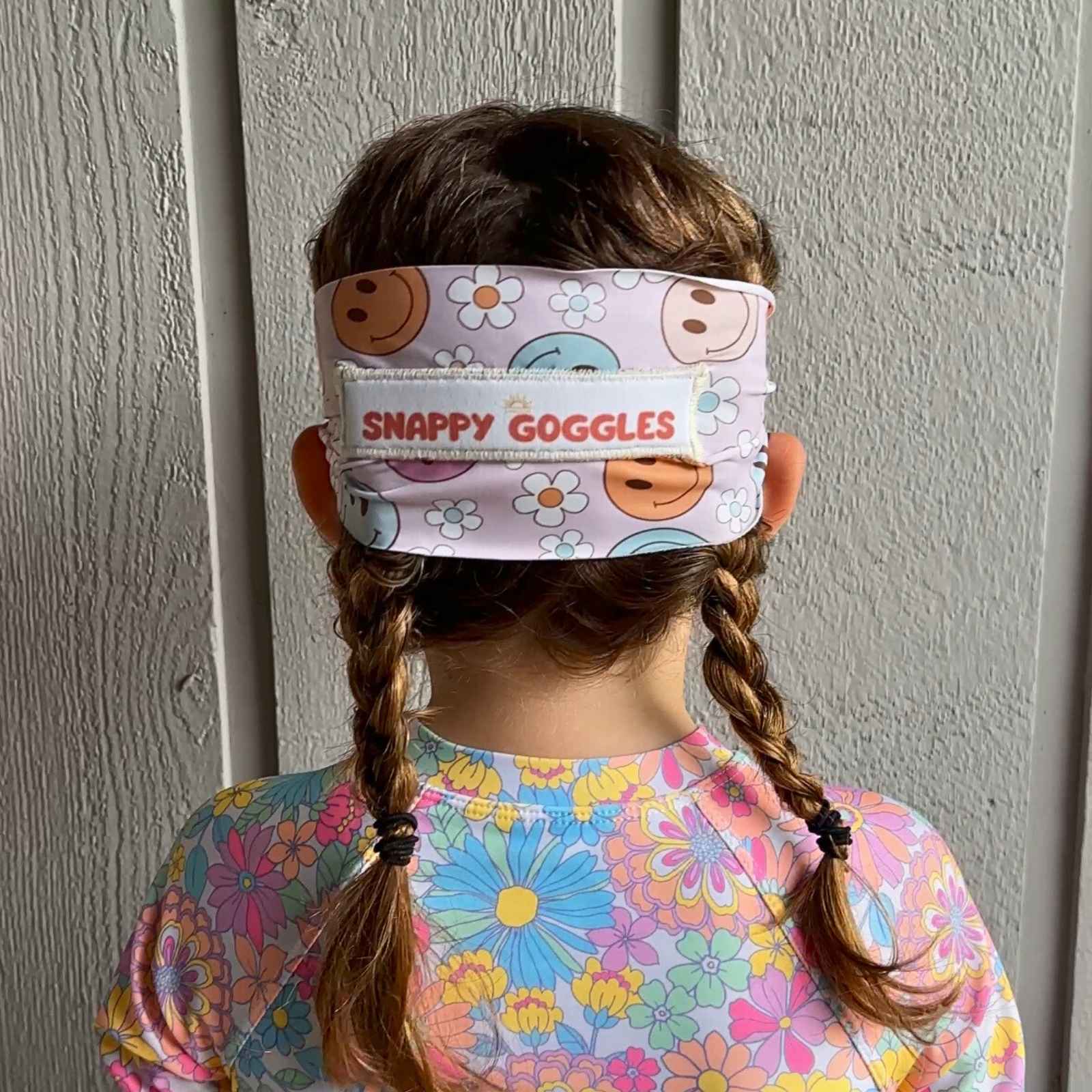 back view of purle orange and blue smiley faces with white flowers kid swim goggles with adjustable, fabric strap – Snappy Goggles