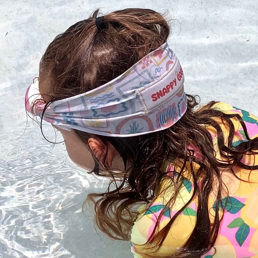 Girl wearing a colorful fabric strap swim goggles on her head with 'Snappy Goggles' branding, sitting in the pool.