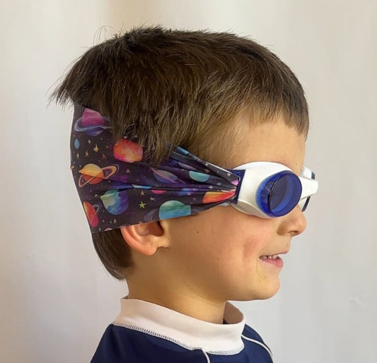 Child wearing colorful space-themed swim goggles with a adjustable, fabric strap. Snappy Goggles