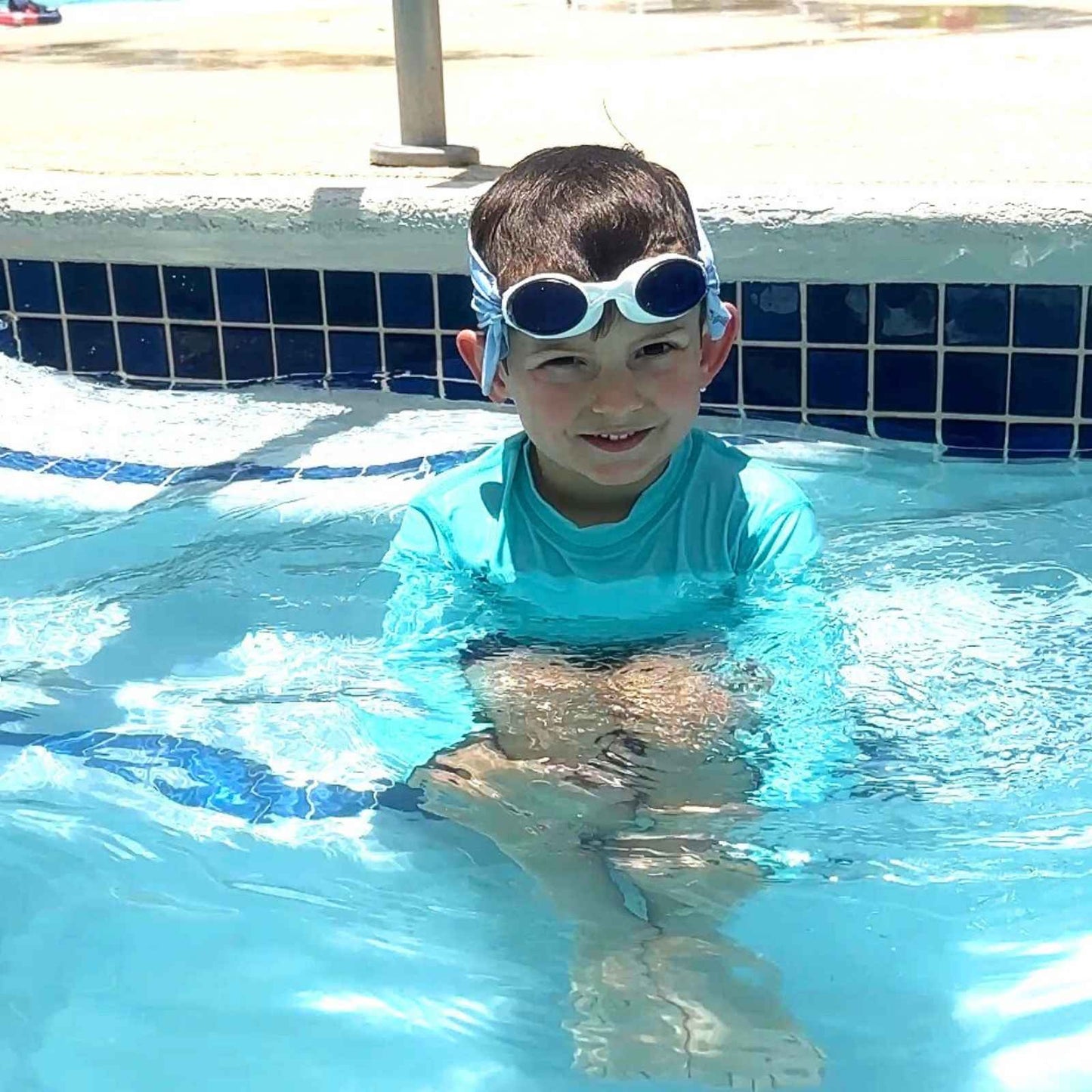 Child in a pool wearing shark attack fabric strap swim goggles and a blue shirt. - Snappy Goggles